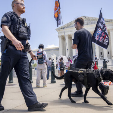 A U.S. Capitol Police officer and K-9 patrol pass protesters by the Supreme Court, Monday, July 1, 2024, after court decisions were announced in Washington. (AP Photo/Jacquelyn Martin)